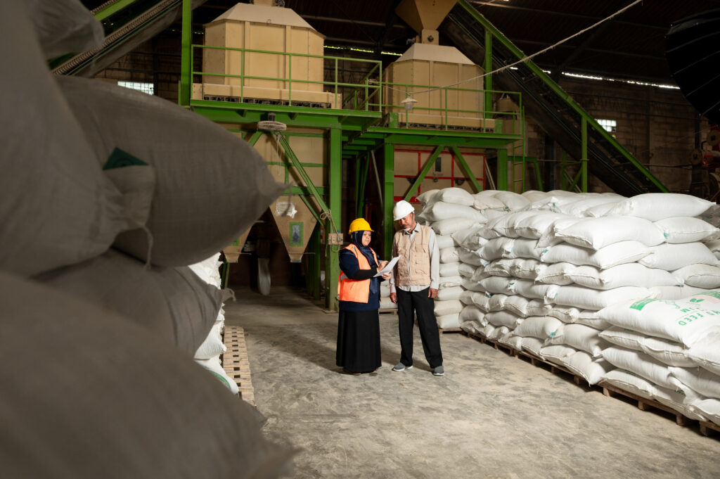Two people reading report with sacks of poultry feed in the background